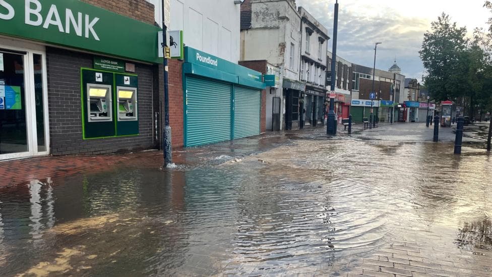 A street with shops along the left and flood water pooling outside.