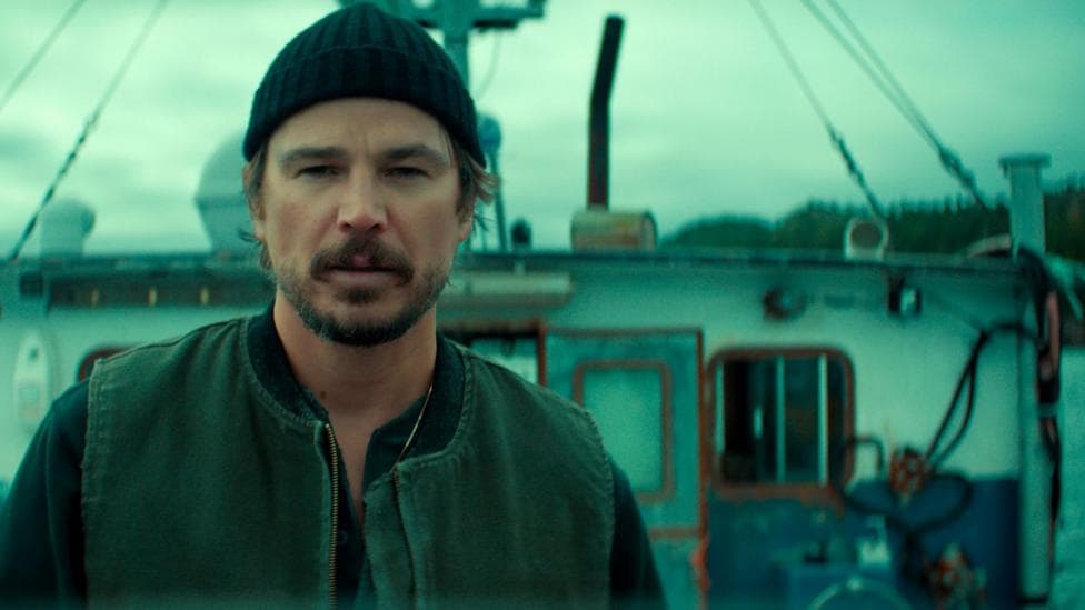An actor dressed as a fisherman stands on a boat looking pensive.