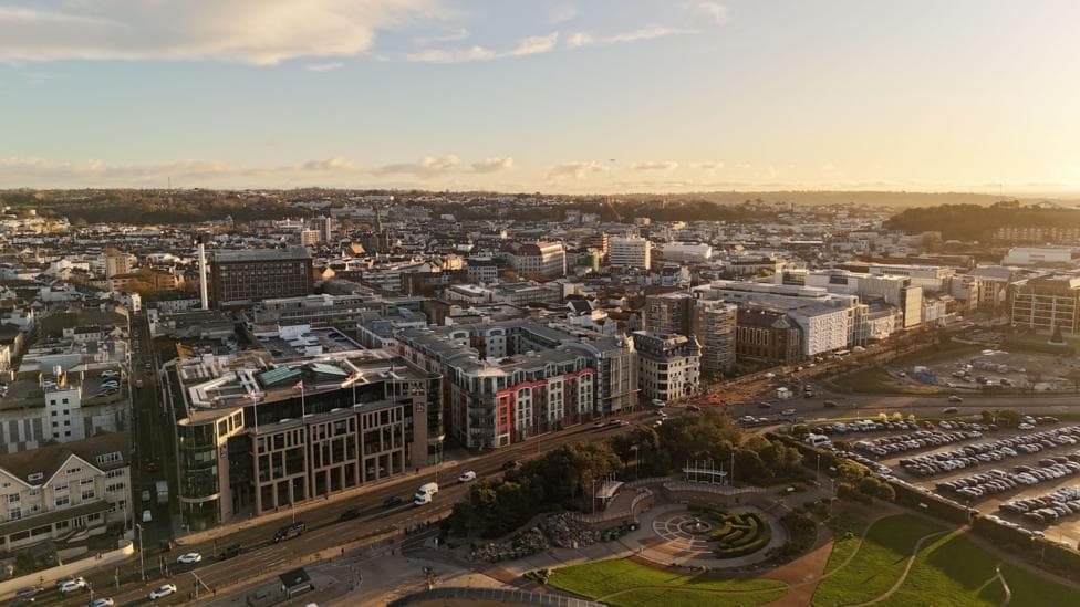 A drone shot of St Helier, Jersey. It shows buildings along a road. Behind there are many more buildings stretching off into the distance